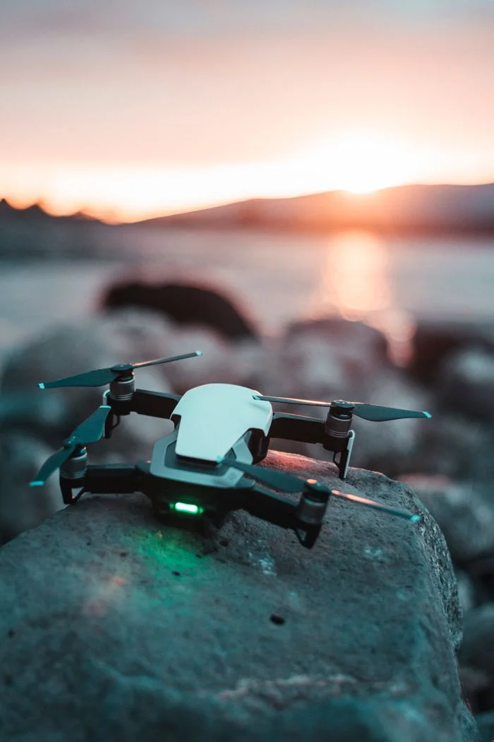 Mastering the First Impression: Your intriguing post title goes here A drone sits on rocky terrain with a vibrant sunset reflecting over water.